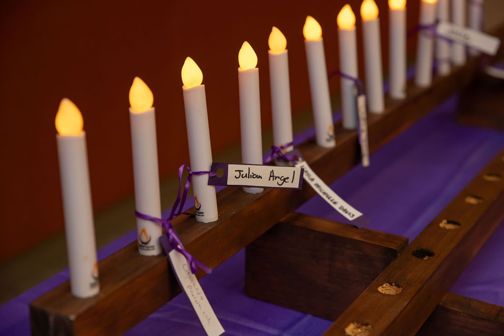 A row of candles with nametags tied to them in purple ribbons.